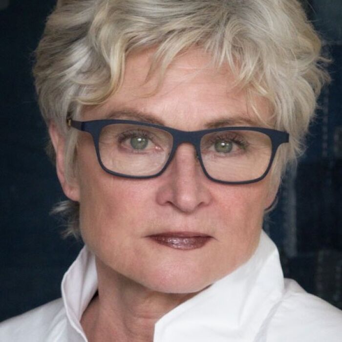 Portrait of an artist mom with short blonde hair and glasses, representing a shocking family tragedy involving her sons and daughter-in-law.