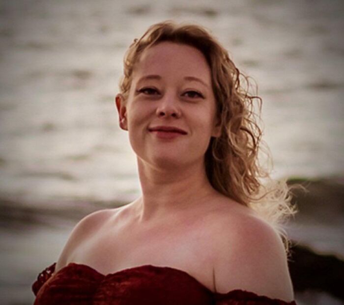 Woman with curly hair wearing a red off-shoulder dress near water, related to Trump cold-blooded insult and fatal ICE shooting.
