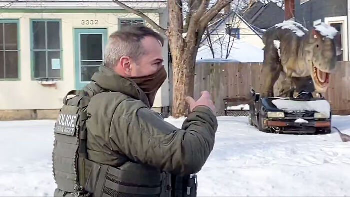 Police officer in tactical gear gestures outside a snow-covered house during a tense moment involving Kristi Noem.