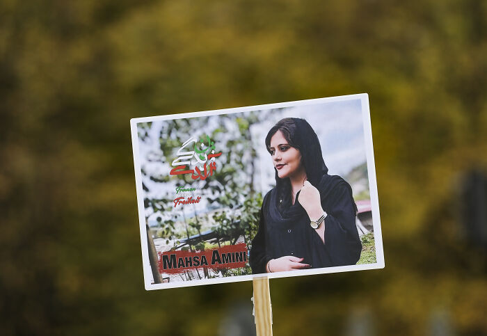 Photo of a protester holding a sign with an image of Mahsa Amini, symbolizing Iran protests and US locked and loaded warning.