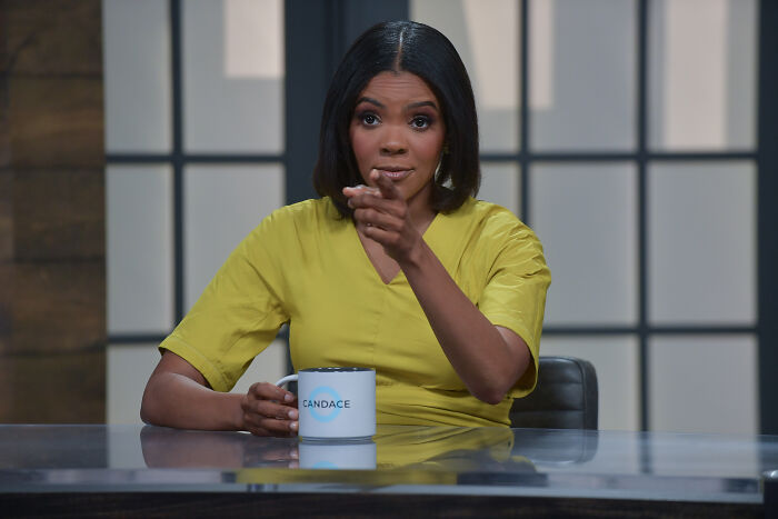 Woman in yellow blouse holding a mug, speaking during a studio discussion on Erika Kirk celebrating Charlie Kirk sales.