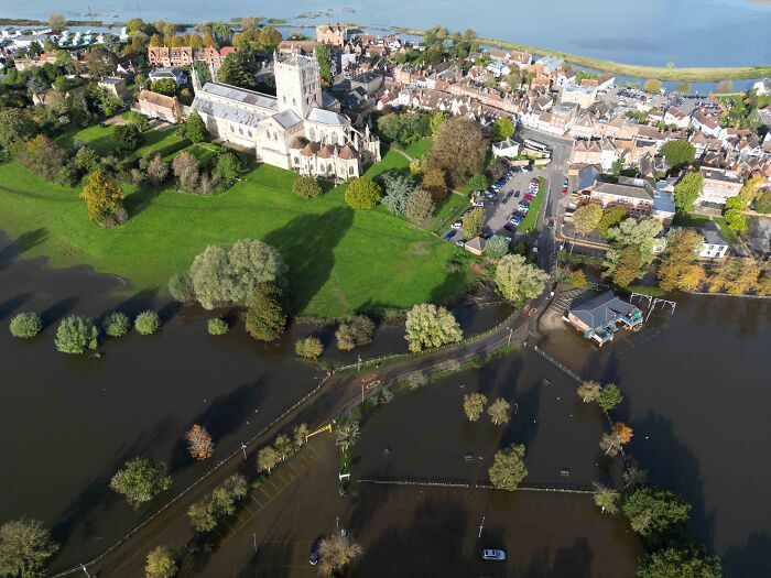 Aerial view of a flooded village with submerged roads and green spaces affected by water overflow after heavy rain.