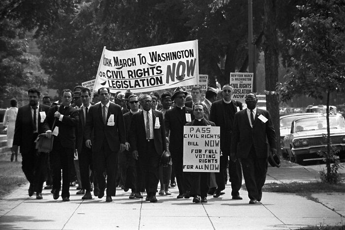 Civil rights marchers walking with signs advocating for civil rights legislation and voting rights on a city street.