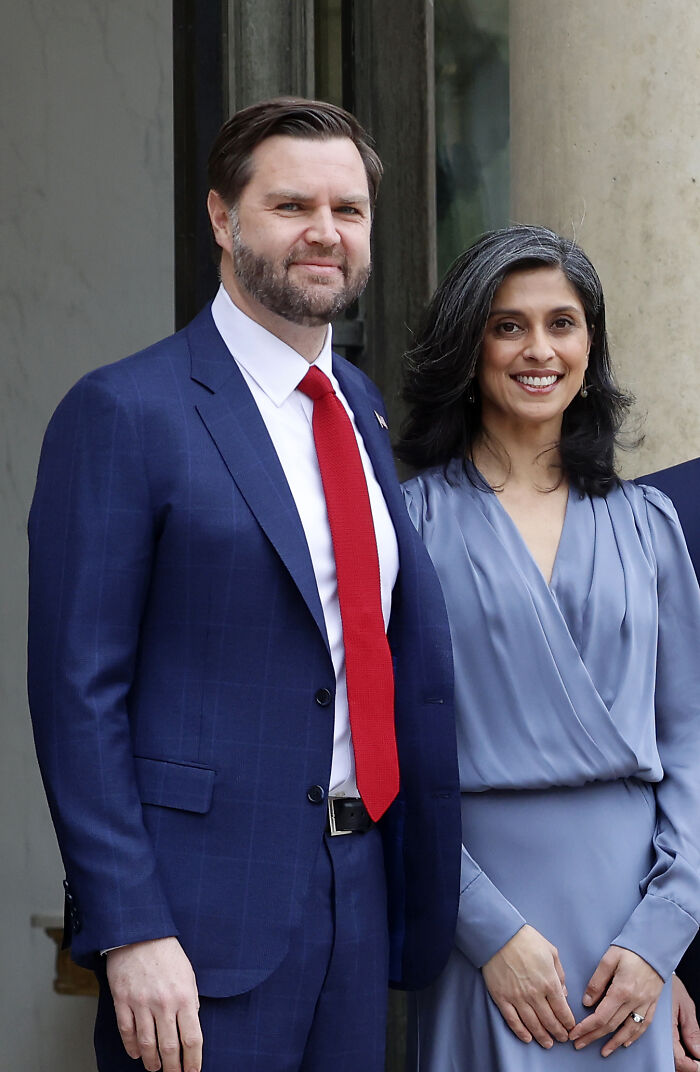 Usha Vance smiling in a blue dress standing next to a man in a blue suit and red tie announcing fourth pregnancy news.