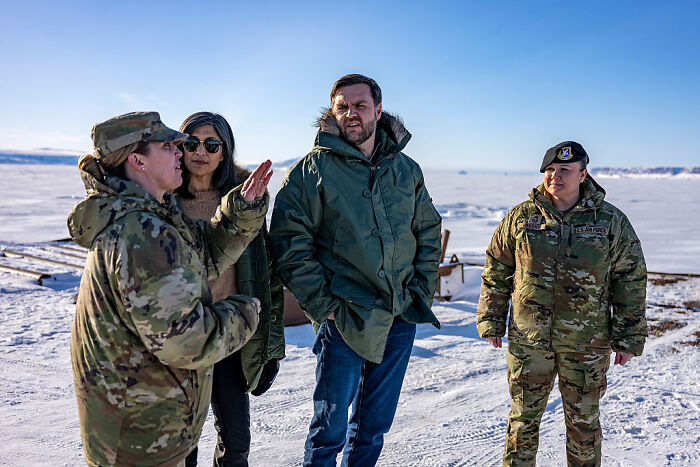 Four people standing outdoors on snow-covered ground, discussing US military presence and Peace President Trump actions.