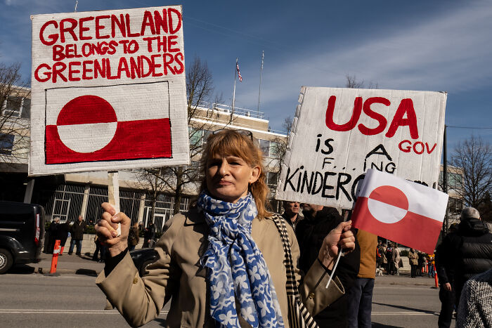 Protester holding Greenland flags and signs amid Trump issues Greenland deadline and PM's strong response.