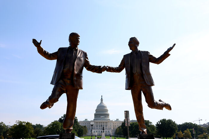 Bronze statues of two men holding hands with the U.S. Capitol in the background on the National Mall.