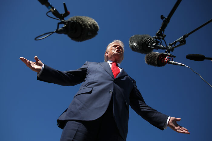 Donald Trump speaking to multiple microphones outdoors, capturing his reaction that went viral on social media.