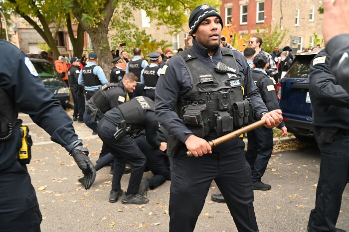 Police officers in tactical gear managing a chaotic street scene during a backlash against a Trump voter seeking advice.