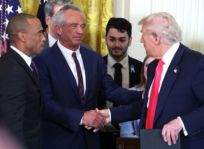 White House officials shaking hands during a surprise war announcement event in a formal room with flags and curtains.