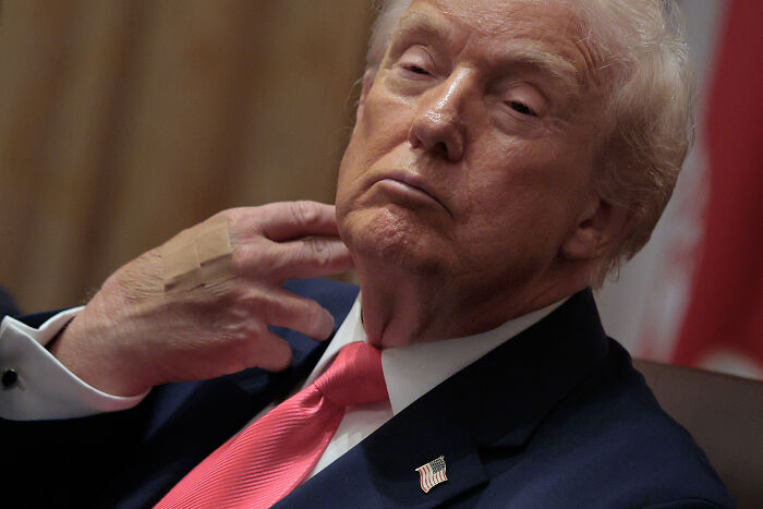 Donald Trump appearing reflective indoors, highlighting use of makeup and compression socks to mask health issues.