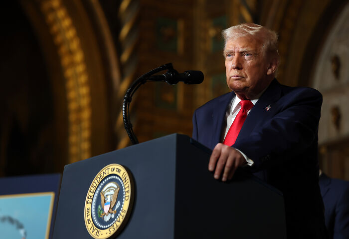 Older man at presidential podium in suit and red tie, stern expression, referencing impeachment concerns