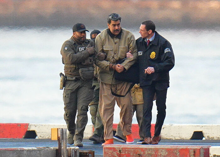 Man in handcuffs escorted by law enforcement officers near water, illustrating lawmakers move to block invasion of NATO territory.