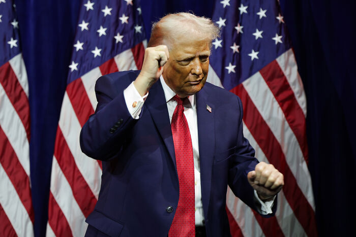 Donald Trump gestures during a speech with American flags in the background, related to peace prize offer news.