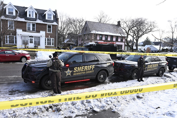 Police officers stand by sheriff vehicles at a crime scene with yellow tape investigating tragic fatal shooting involving ICE.