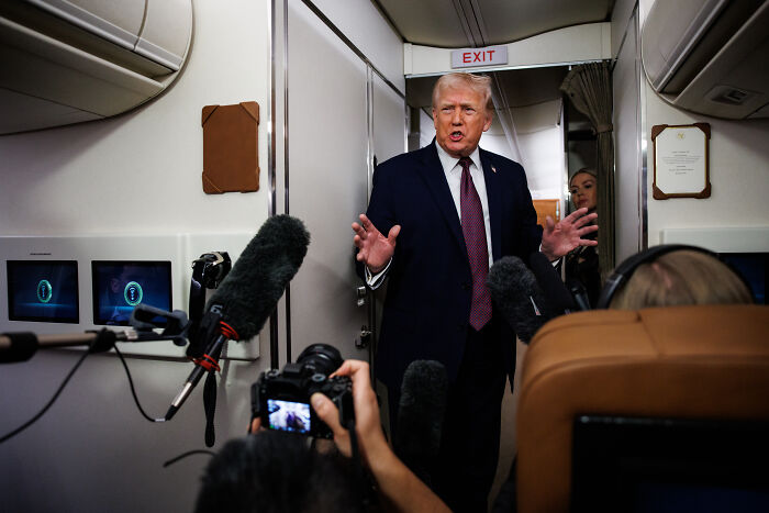 Former president Trump speaking on a plane, surrounded by microphones, addressing ICE officer immunity questions.
