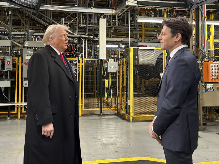 Donald Trump speaking with a man in a factory setting, related to message on Renee Nicole Good's fatal shooting case.