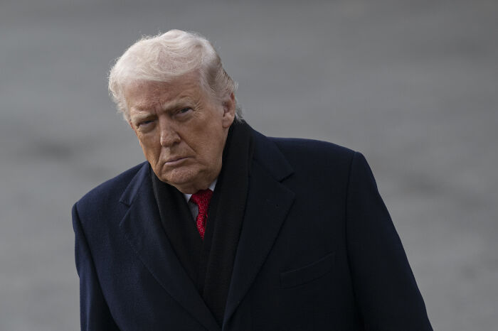 Former President Trump outdoors wearing a dark coat and red tie, with a serious expression, related to peace statement.