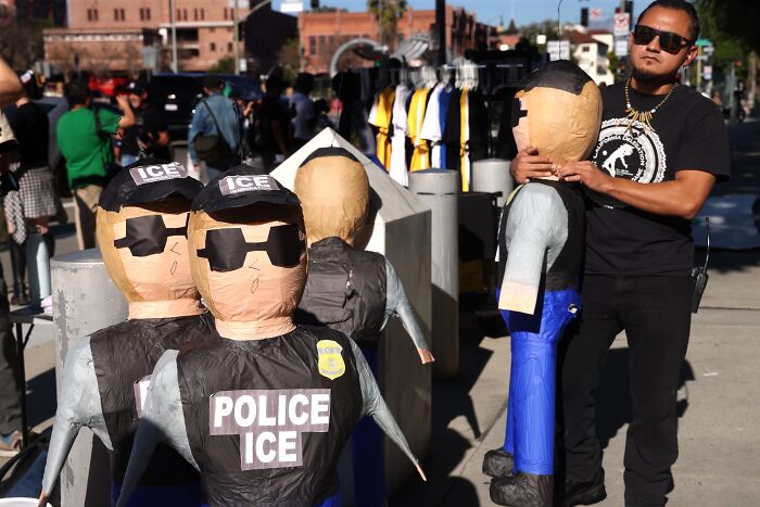 Man setting up police ICE officer mannequins on a city street highlighting backlash over deploying ICE at the Olympics.
