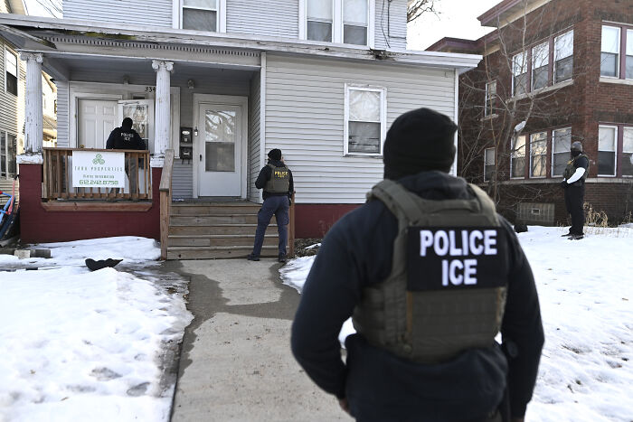 ICE police officers in tactical gear outside a residential house in winter, reflecting issues related to being American after Trump.