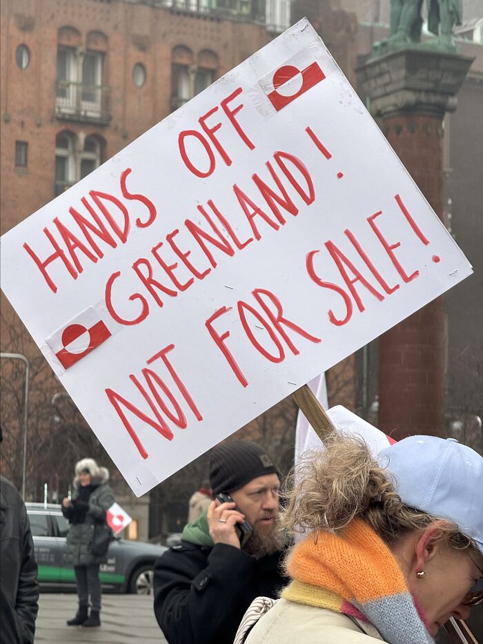 Protester holding a sign saying Hands Off Greenland Not For Sale during a public demonstration in a city square.