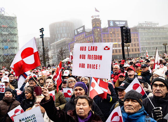 Crowd holding flags and signs at a protest, illustrating themes related to Trump&rsquo;s anti-democracy agenda and radical plans.