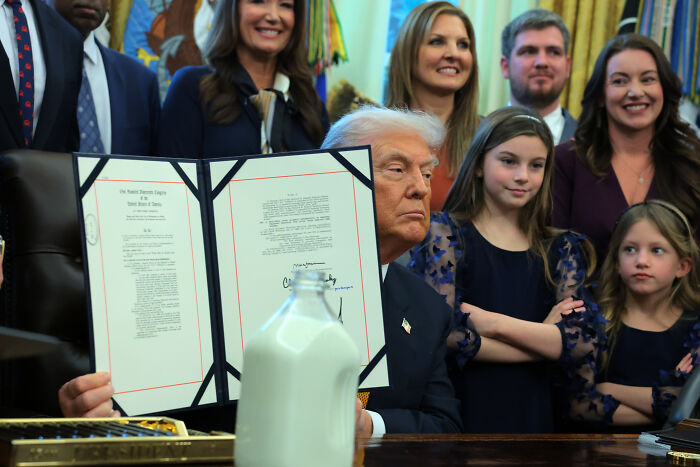 Donald Trump holding a signed document with a bottle of whole milk in the foreground during a public event.