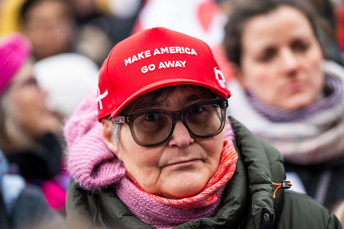 Greenland resident wearing a red MAGA hat that says Make America Go Away, dressed warmly in winter clothing at an outdoor event.