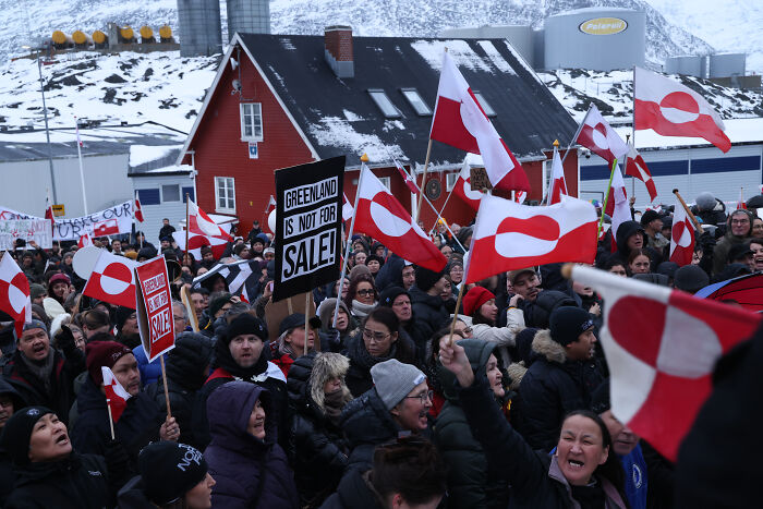 Greenland residents protesting with flags and signs in cold weather, highlighting local resistance and community unity.