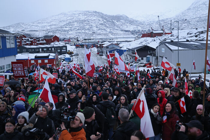 Crowd protesting in Greenland with flags and signs, capturing the viral urban yoga video hitting a nerve with the MAGA crowd.