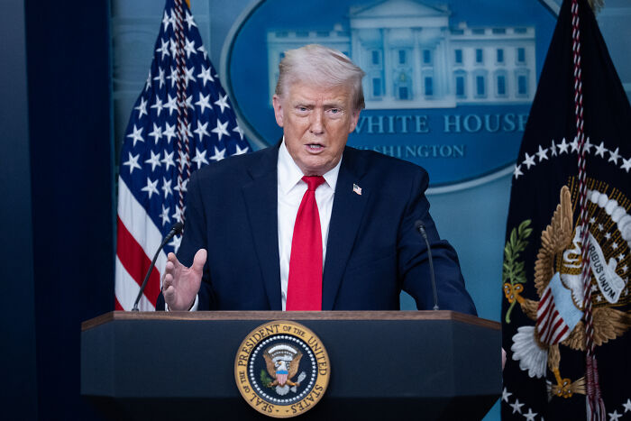 Former U.S. president speaking at White House podium with flags, related to Greenland trolls viral urban yoga video topic.