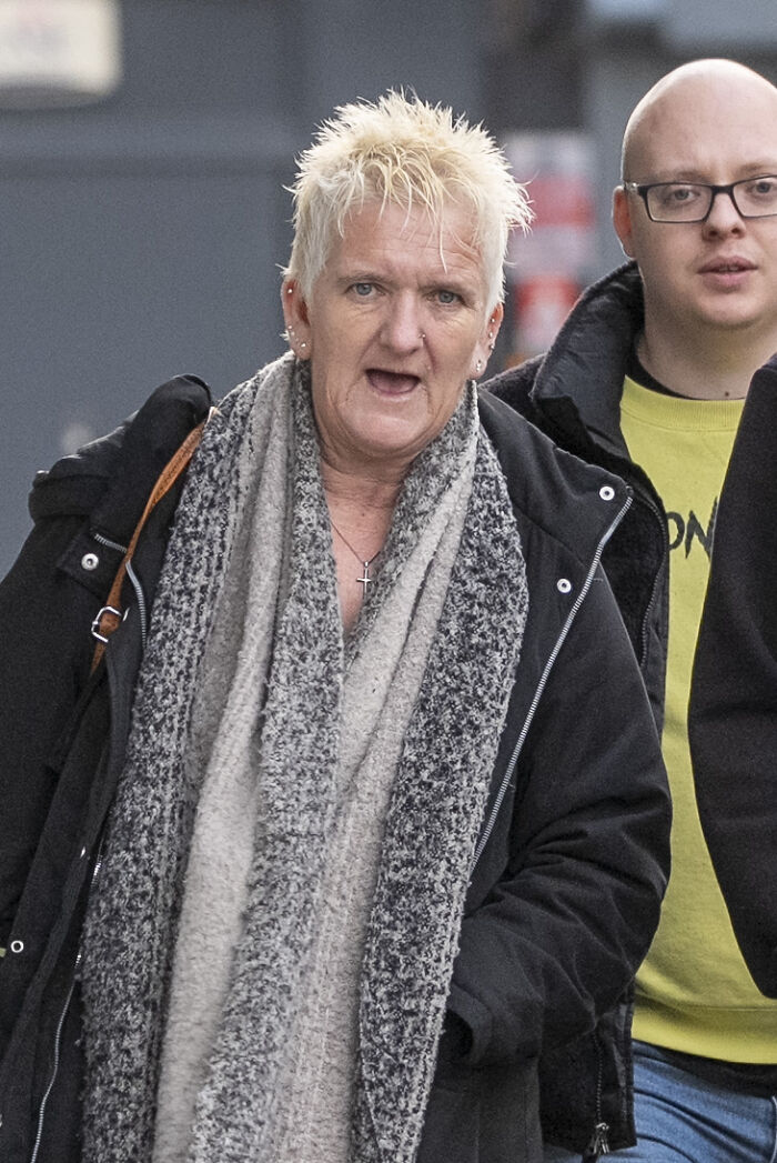 Woman vulnerable and imprisoned, wearing a gray scarf and black coat, walking outdoors during daytime.