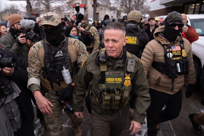 Border Patrol Chief Greg Bovino in tactical gear walking through a crowd during a high-profile removal event.