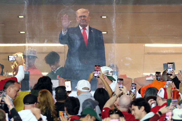 Trump appears in a stadium box while crowd reacts with boos and records on their phones during the national anthem at CFP final.