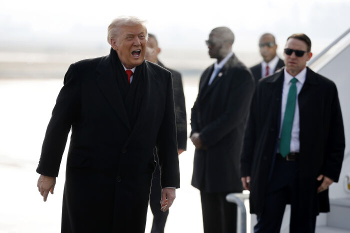 Donald Trump wearing a black coat speaking outdoors with security personnel behind him at an event in Davos.