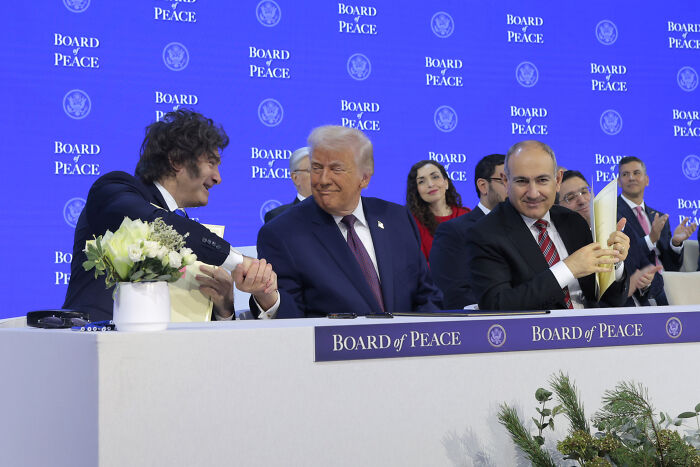 Donald Trump attempts power handshake at Davos event while attendees notice a pair of shoes in the background.