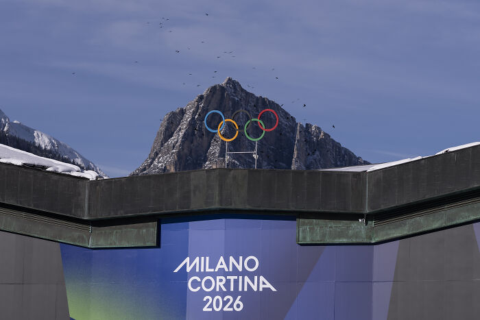 Olympic rings above Milano Cortina 2026 sign with mountain background, linked to Trump ICE deployment plan controversy.