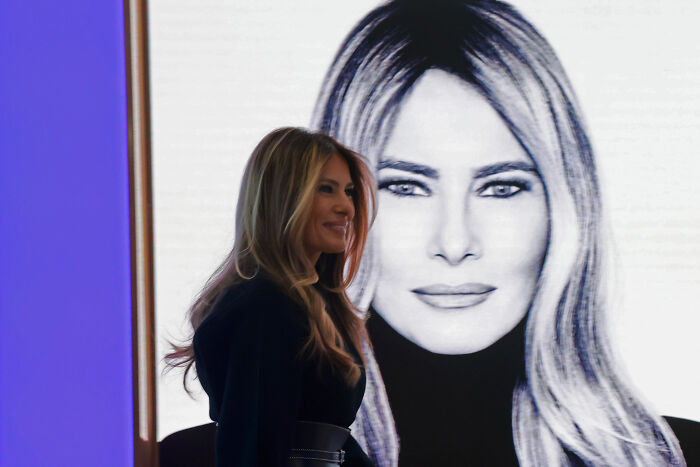 Melania Trump standing near a large black and white portrait of herself at a public event.