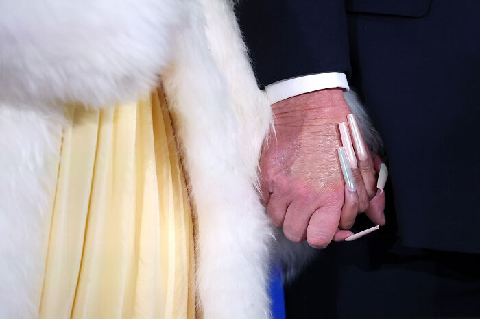 Close-up of hands holding, featuring long acrylic nails and a white fur coat, related to Nicki Minaj MAGA and Trump discussion.