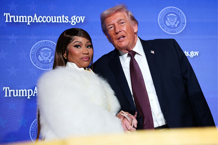 Nicki Minaj and Donald Trump posing together at an event with TrumpAccounts.gov signs in the background.