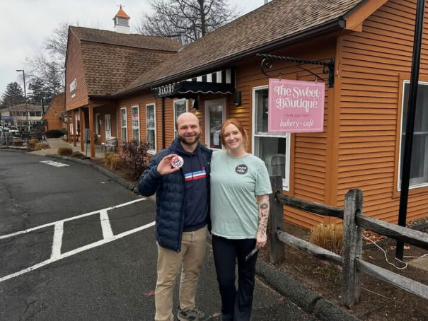 Two bakery owners standing outside The Sweet Boutique holding anti-ICE cookies after receiving vile threats.