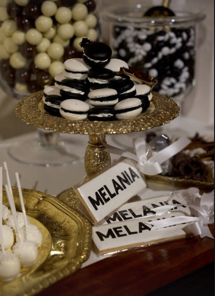 Black and white macarons on a gold stand with Melania-themed cookies displayed on a dessert table at a screening event.