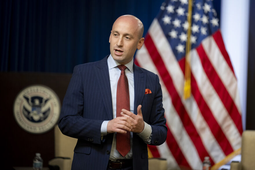 Stephen Miller speaking in front of American flags, related to Kristi Noem political strategy discussion.