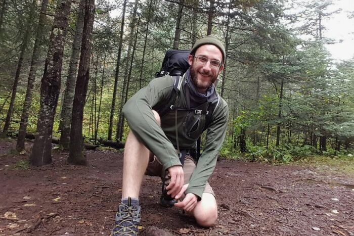 Alex Pretti wearing glasses and outdoor gear, smiling and crouching in a forest, days before clashing with federal agents.