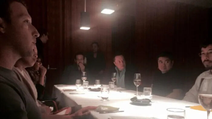 Group of people sitting around a dimly lit table, engaged in serious discussion, related to MAGA influencers and Epstein ties.