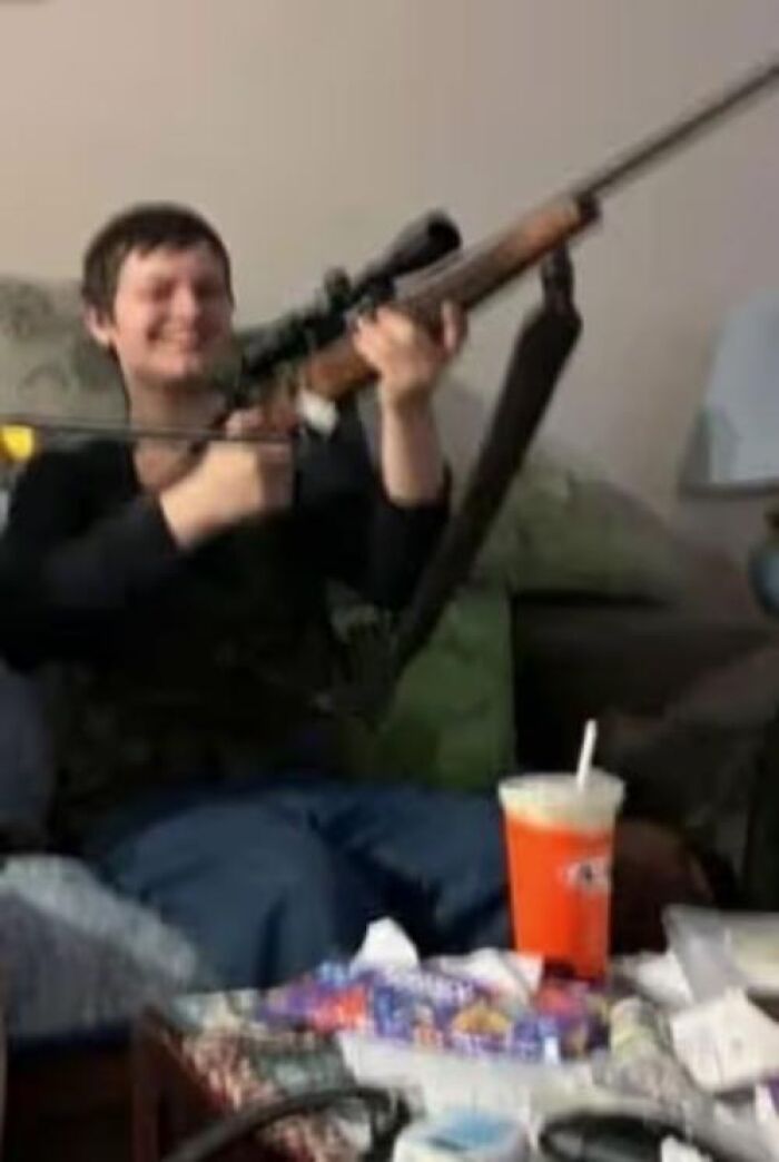 Alt text: Young man holding a scoped rifle indoors, related to families honoring children lost in Canada school attack.
