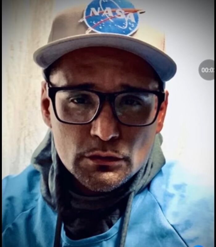 Man wearing glasses and a NASA hat in a close-up, representing family lawsuit after prison attack viral on social media.