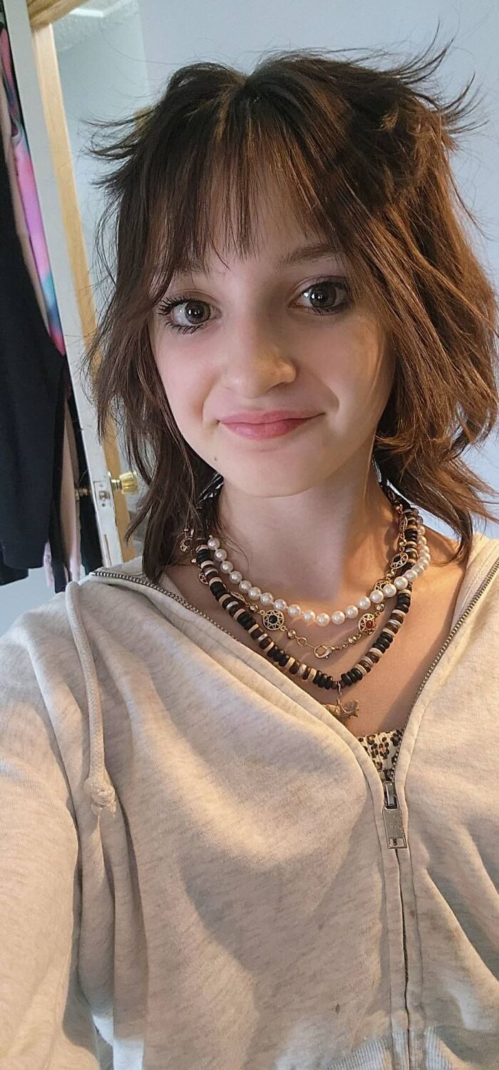 Young girl wearing layered necklaces and a light hoodie, symbolizing families honoring children lost in Canada school attack.