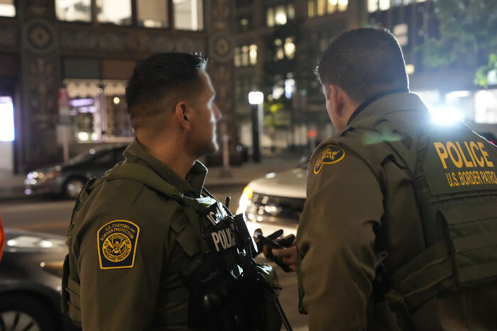 Minneapolis immigration agents in uniform discussing operations at night with body cameras visible on their gear.