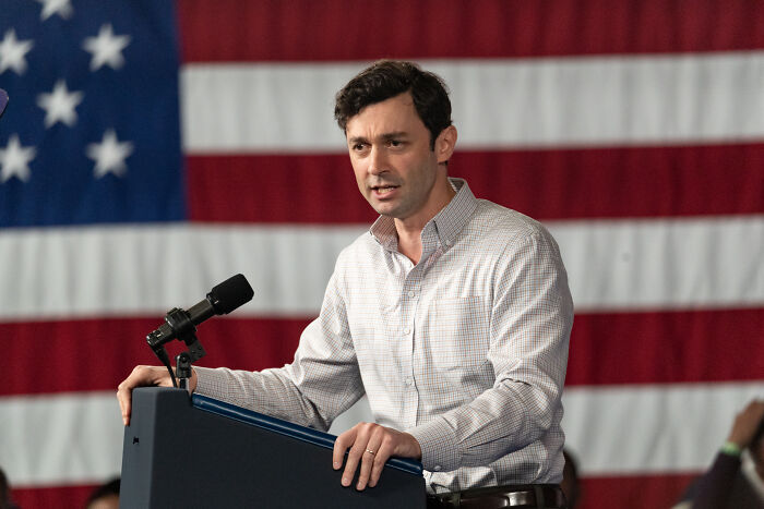 Young senator delivering a speech with an American flag backdrop during a scathing Trump comparison event.